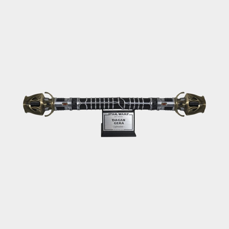 May include: A black lightsaber with gold accents and a silver blade. The lightsaber is on a stand with a silver plaque that reads "STAR WARS: The Black Series DAGAN GERA LIGHTSABER".