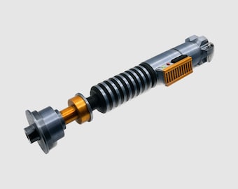 May include: A silver and black lightsaber with a gold handle and a black and orange control panel. The lightsaber is a popular toy for fans of the Star Wars franchise.