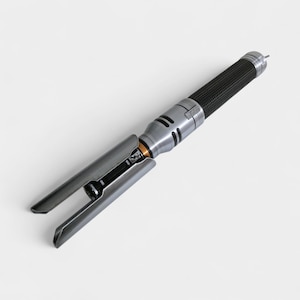 May include: A silver and black lightsaber with a textured black grip and a silver blade guard. The lightsaber has a detailed design with a metallic finish and a futuristic aesthetic.