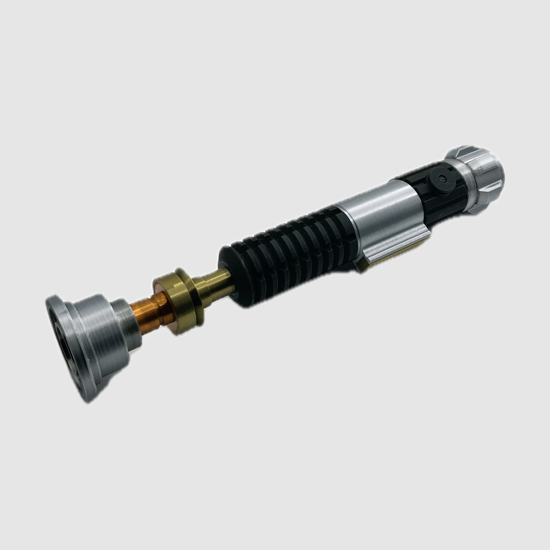 May include: A cylindrical metal prop handle featuring a silver emitter, a central copper-colored neck section, and a black ribbed grip. The handle includes a silver and black control box with a circular button and a silver pommel at the end.