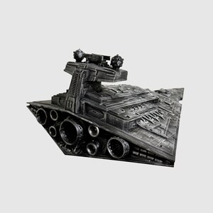 May include: A detailed, dark gray model of a Star Destroyer spaceship. The model features intricate surface details, multiple engine ports, and a prominent command tower with spherical turrets. The ship's design is angular and industrial, with a textured finish.