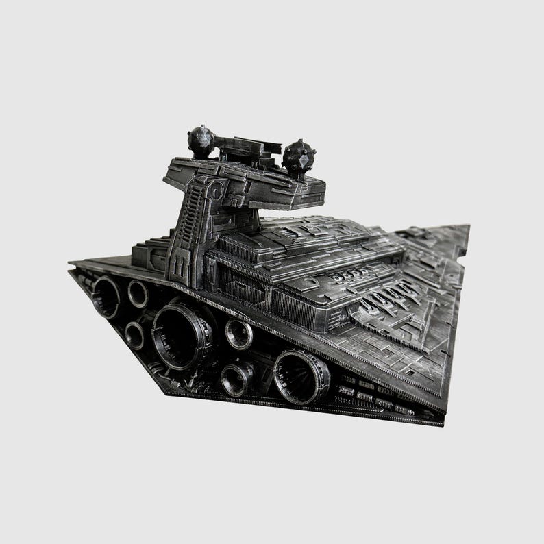 May include: A detailed, dark gray model of a Star Destroyer spaceship. The model features intricate surface details, multiple engine ports, and a prominent command tower with spherical turrets. The ship's design is angular and industrial, with a textured finish.