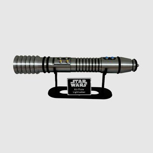 May include: A silver lightsaber with a black stand and a silver plaque that reads "STAR WARS Kit Fisto Lightsaber".