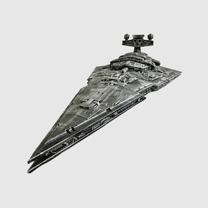 May include: A detailed, metallic gray model of a Star Destroyer spaceship. The model features intricate surface detailing, a prominent command tower, and a distinctive wedge shape. The ship is angled, showcasing its length and design.