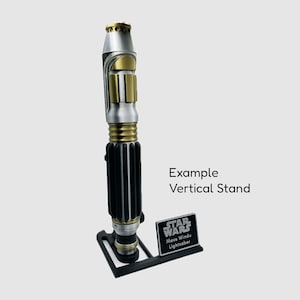May include: A silver and gold lightsaber with a black handle, displayed on a black stand with a black plaque that reads "STAR WARS Mace Windu Lightsaber". Example Vertical Stand.