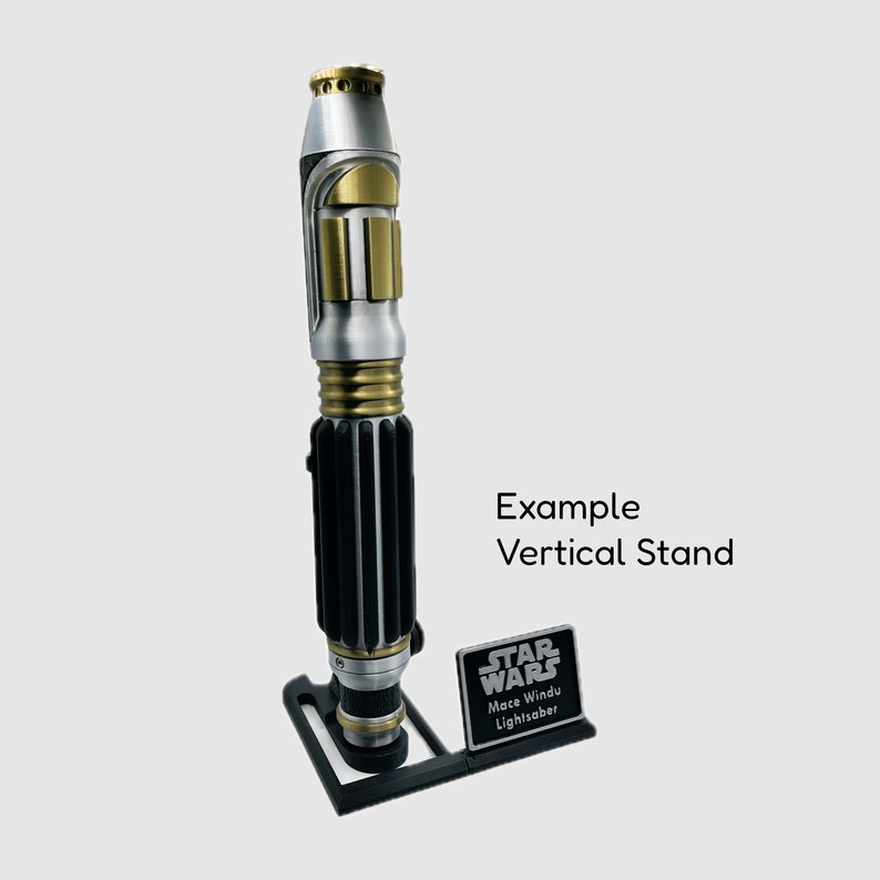 May include: A silver and gold lightsaber with a black handle, displayed on a black stand with a black plaque that reads "STAR WARS Mace Windu Lightsaber". Example Vertical Stand.