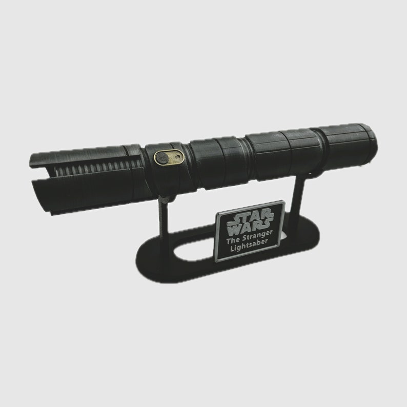 May include: A black lightsaber with a gold button on the handle, displayed on a black stand with a silver plaque that reads "Star Wars The Stranger Lightsaber".