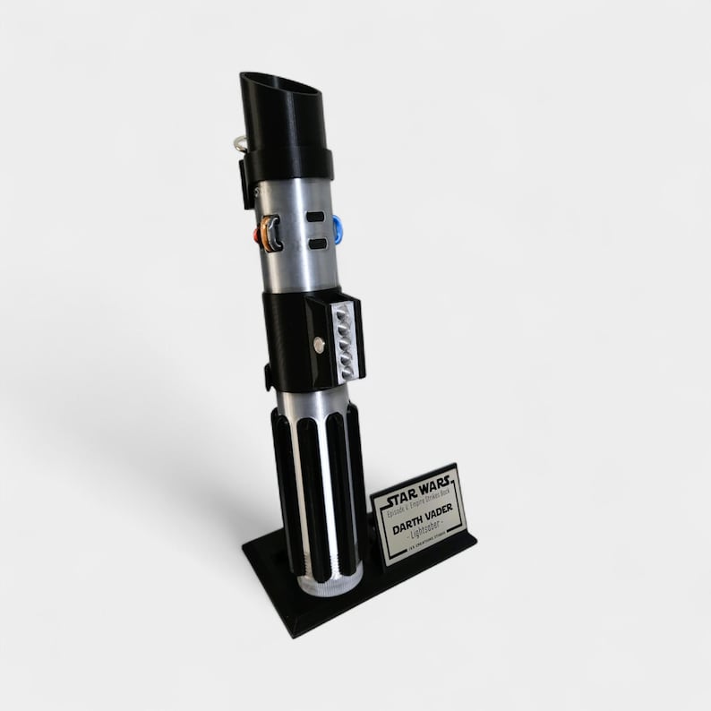 May include: A replica of Darth Vader's lightsaber, featuring a black handle and silver accents. The lightsaber is mounted on a black base with a small plaque that reads "STAR WARS Darth Vader Lightsaber". The lightsaber is a prop from the Star Wars franchise.