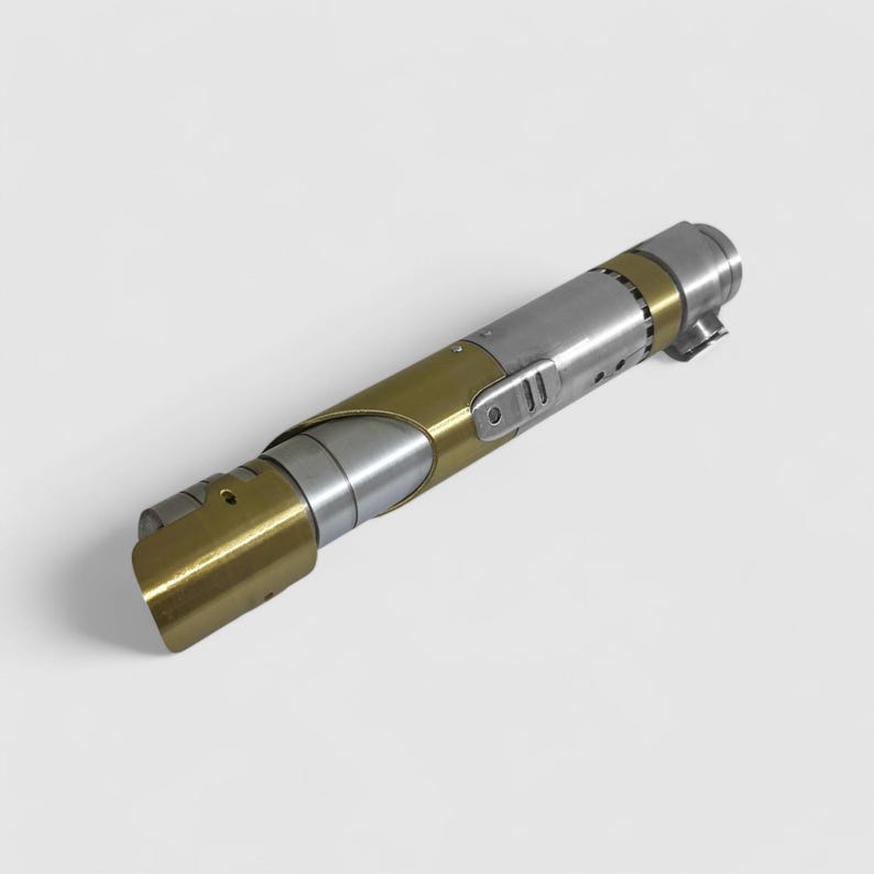 May include: A silver and gold lightsaber with a black handle and a silver blade. The lightsaber is a popular prop from the Star Wars franchise.