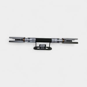 May include: A silver and black lightsaber with a black handle, displayed on a black stand. The lightsaber has a textured grip and silver accents. The stand has a Star Wars logo and text that reads "Cal Kestis Lightsaber."
