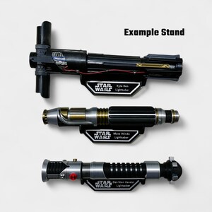 May include: Three Star Wars lightsabers, including Kylo Ren, Mace Windu, and Obi-Wan Kenobi models, displayed on black stands. The lightsabers are black, silver, and gold, with intricate detailing. The stands feature the Star Wars logo and character names.