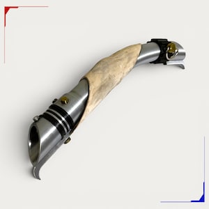 May include: A curved metal hilt featuring a polished silver finish with a textured, light-coloured organic grip section. The design includes black grooved accents, small gold-toned circular buttons, and a metallic ring attachment at the end.