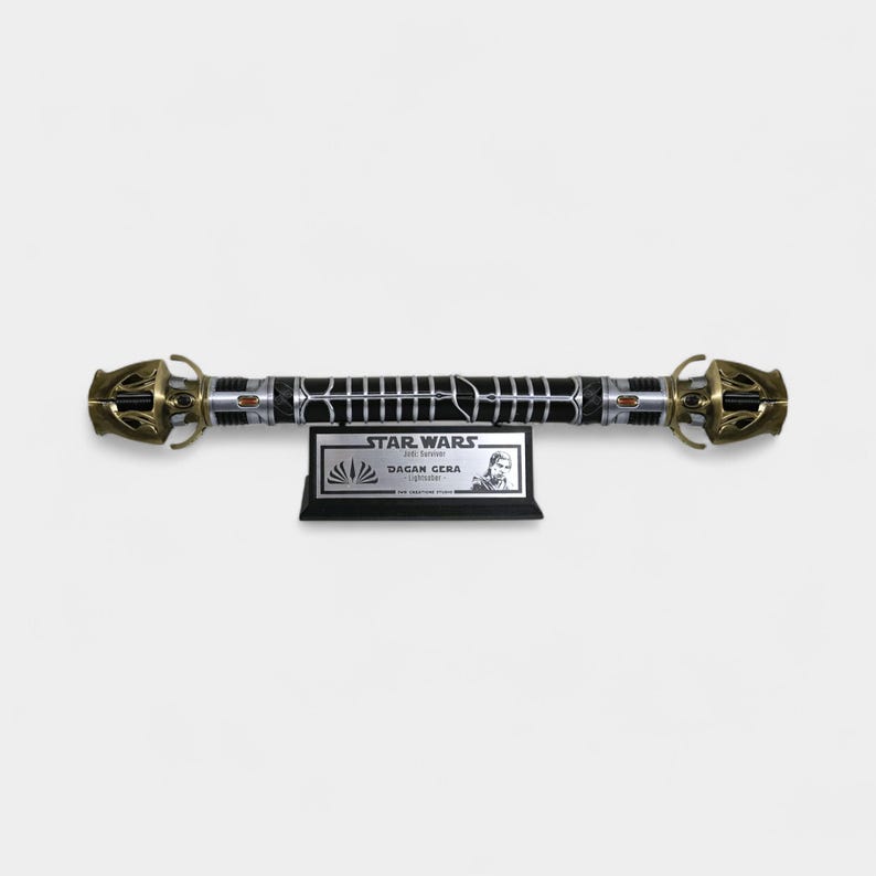 May include: A black lightsaber with gold accents and a silver blade. The lightsaber is on a black display stand with a silver plaque that reads "STAR WARS: JEDI SURVIVOR - DAGAN GERA - LIGHTSABER".