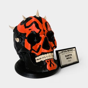 Op de afbeelding: Een zwart en rood schedelbeeld met witte tanden en hoorns. De sculptuur is gebaseerd op het Star Wars-personage Darth Maul. Een klein plaatje ernaast luidt "STAR WARS Darth Maul - Skull."