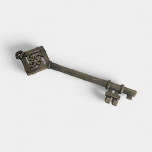 May include: An antique-style key with a decorative square head featuring an ornate floral design. The key has a twisted stem and a detailed bit. The metal key is a bronze color and appears to be made of cast iron.