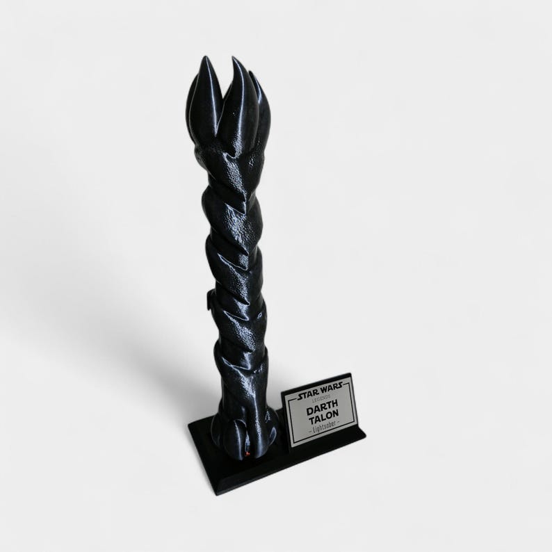 May include: A black Darth Talon lightsaber replica from Star Wars. The lightsaber has a twisted, textured design with a claw-like top. It stands on a black base with a small sign that reads "Star Wars Darth Talon Lightsaber".