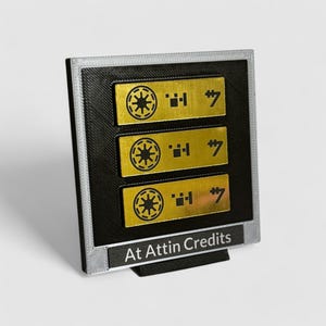 May include: A black and silver display stand with three gold rectangular plaques. Each plaque features a black symbol, a black number "7", and the text "At Attin Credits".