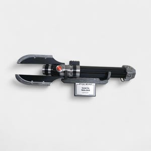 May include: A black and silver Darth Malgus lightsaber prop, with a red button and a silver blade guard. The lightsaber is mounted on a gray stand with a Star Wars label.