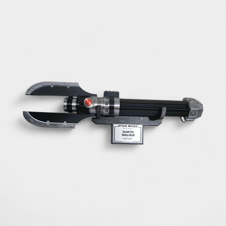 May include: A black and silver Darth Malgus lightsaber prop, with a red button and a silver blade guard. The lightsaber is mounted on a gray stand with a Star Wars label.
