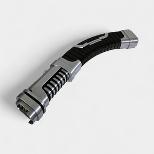 May include: A futuristic-looking, curved lightsaber with a black grip and silver accents. The handle features a series of vertical ridges and a silver button. The blade end has a rectangular opening. The overall design suggests a sci-fi or fantasy theme.