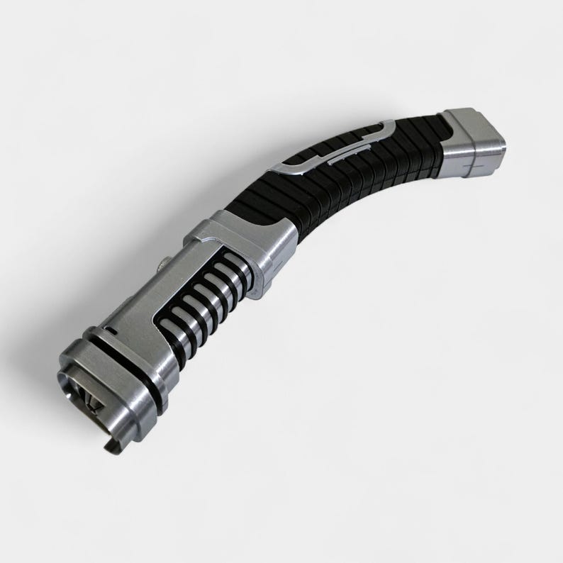 May include: A futuristic-looking, curved lightsaber with a black grip and silver accents. The handle features a series of vertical ridges and a silver button. The blade end has a rectangular opening. The overall design suggests a sci-fi or fantasy theme.