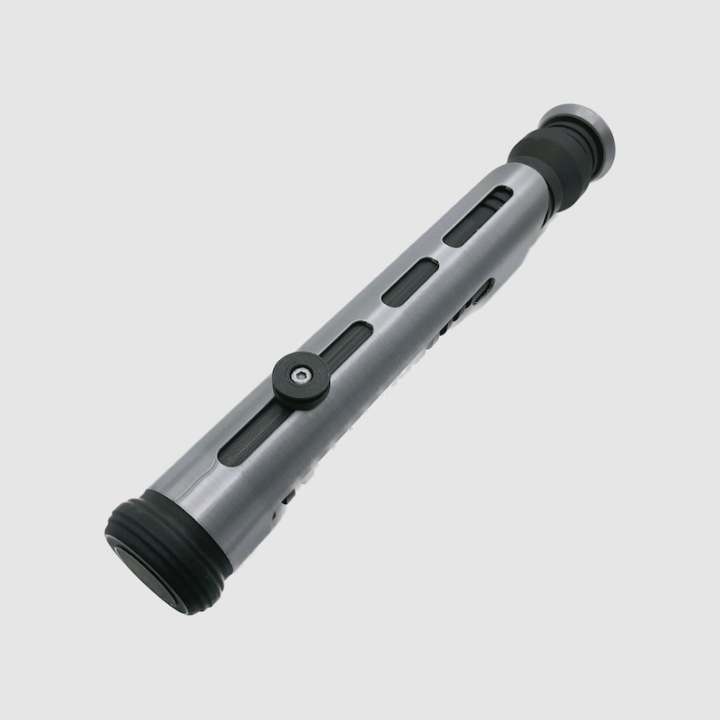 May include: A silver and black lightsaber prop with a textured surface and a black button on the side.