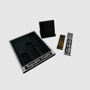 May include: A black plastic tray with three rectangular slots labeled "Republic Credits". The tray is next to three rectangular plastic tokens, one gold and two silver.