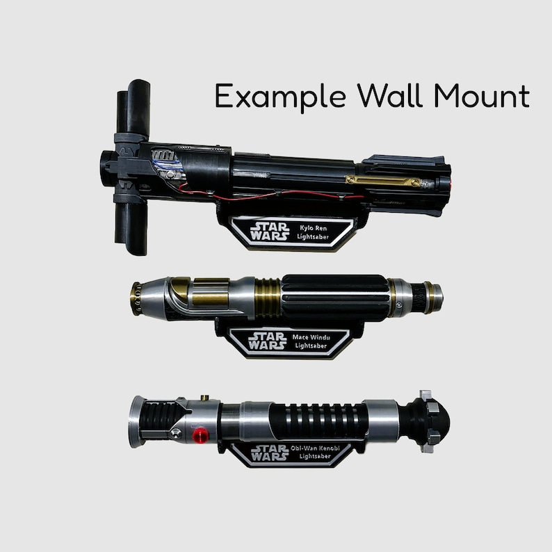 May include: Three Star Wars lightsabers mounted on a wall. The lightsabers are black, silver, and gold. The wall mount is silver and has the Star Wars logo on it. The lightsabers are labeled with the names of the characters they belong to: Kylo Ren, Mace Windu, and Obi-Wan Kenobi.