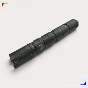 May include: A cylindrical black handle with a textured, segmented surface and a diagonal spiral pattern. The object features a small, rectangular brass-coloured switch plate with a black button centred on the side of the main body.
