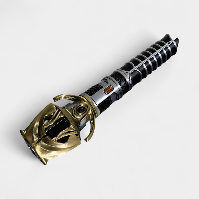 May include: A black and gold lightsaber with a detailed hilt and a black handle. The hilt has a silver accent and a red button.