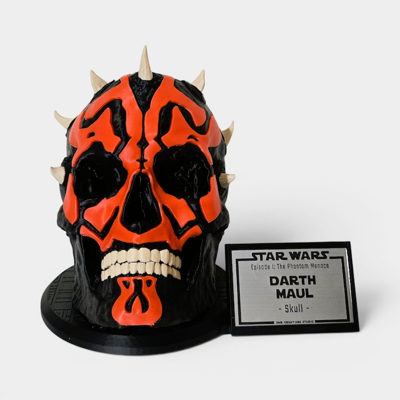 Op de afbeelding: Een zwart en rood Darth Maul schedelbeeld met witte tanden en hoornachtige uitsteeksels. Het beeld staat op een zwarte basis en ernaast staat een zilveren plaatje met de tekst "STAR WARS Darth Maul - Skull".