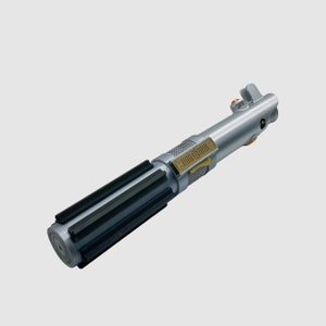 May include: A silver-toned cylindrical prop handle featuring a black-ribbed grip section, a gold-colored rectangular control plate with etched markings, and a small orange circular accent near the top emitter assembly.
