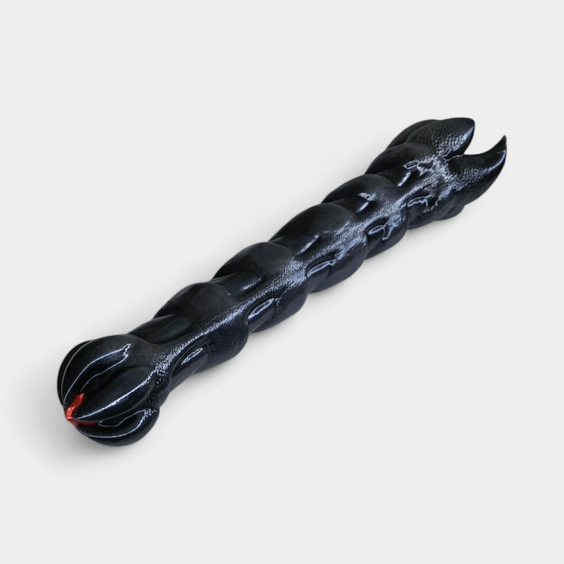 May include: A black, textured, elongated object with a series of rounded segments. One end features a claw-like design, while the other has a rounded shape with a red accent. The object is likely a decorative or functional item.