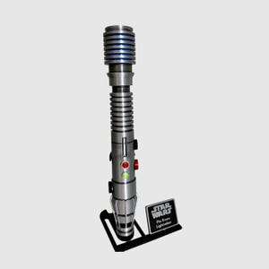 May include: A silver lightsaber with a blue blade and a black stand. The lightsaber has a green and red light on the side. The stand has a black plaque with the text "Star Wars Plo Koon Lightsaber".