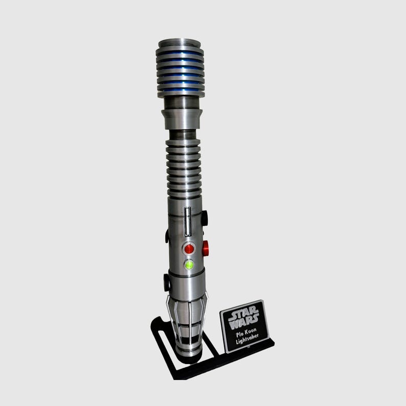 May include: A silver lightsaber with a blue blade and a black stand. The lightsaber has a green and red light on the side. The stand has a black plaque with the text "Star Wars Plo Koon Lightsaber".