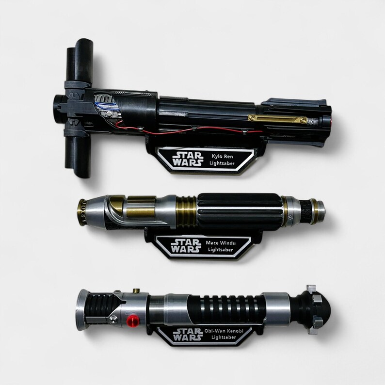 May include: Three Star Wars lightsaber replicas mounted on black display stands with the name of the lightsaber and "Star Wars" printed on each stand.