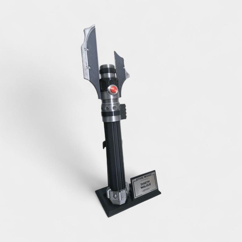 May include: A black and silver Darth Malgus lightsaber replica, standing on a black base. The lightsaber features a red button and intricate detailing. A small plaque with the text "STAR WARS Darth Malgus" is at the base.