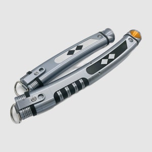 Peut inclure: Deux accessoires cylindriques argent&eacute;s aux corps incurv&eacute;s, dot&eacute;s de sections de pr&eacute;hension noires, d'incrustations m&eacute;talliques en forme de losange et d'un petit accent triangulaire orange &agrave; l'extr&eacute;mit&eacute;. Chaque pi&egrave;ce inclut un anneau m&eacute;tallique.