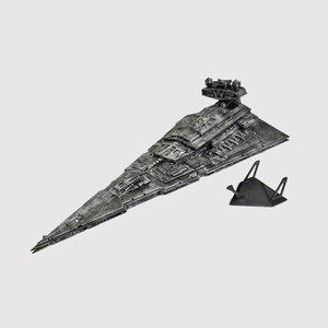 May include: A detailed, metallic gray model of a Star Destroyer spaceship, featuring intricate surface details and a prominent command tower. The model is displayed with a black stand, showcasing its impressive design and scale.