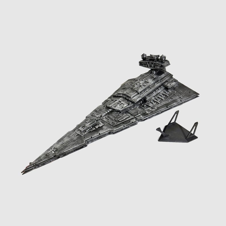 May include: A detailed, metallic gray model of a Star Destroyer spaceship, featuring intricate surface details and a prominent command tower. The model is displayed with a black stand, showcasing its impressive design and scale.