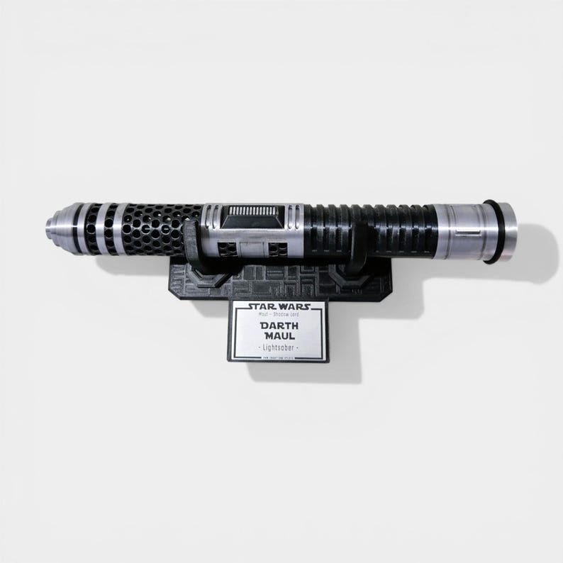 Puede incluir: R&eacute;plica del sable de luz de Darth Maul, con dise&ntilde;o plateado y negro. El sable de luz est&aacute; montado en un soporte negro con una placa que dice "Star Wars - Darth Maul - Lightsaber".