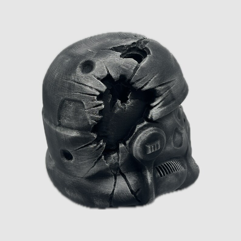 K&ouml;nnte beinhalten: Ein schwarzer, zerbrochener Plastikhelm mit einer rissigen und besch&auml;digten Oberfl&auml;che. Der Helm hat ein Visier und ein kleines, rundes, schwarzes Objekt an der Seite.