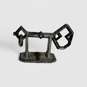 May include: A black metal key replica with intricate details and a decorative base. The key is shaped like a stylized letter 'J' and has a diamond-shaped design in the center. The base is rectangular and has a textured surface.