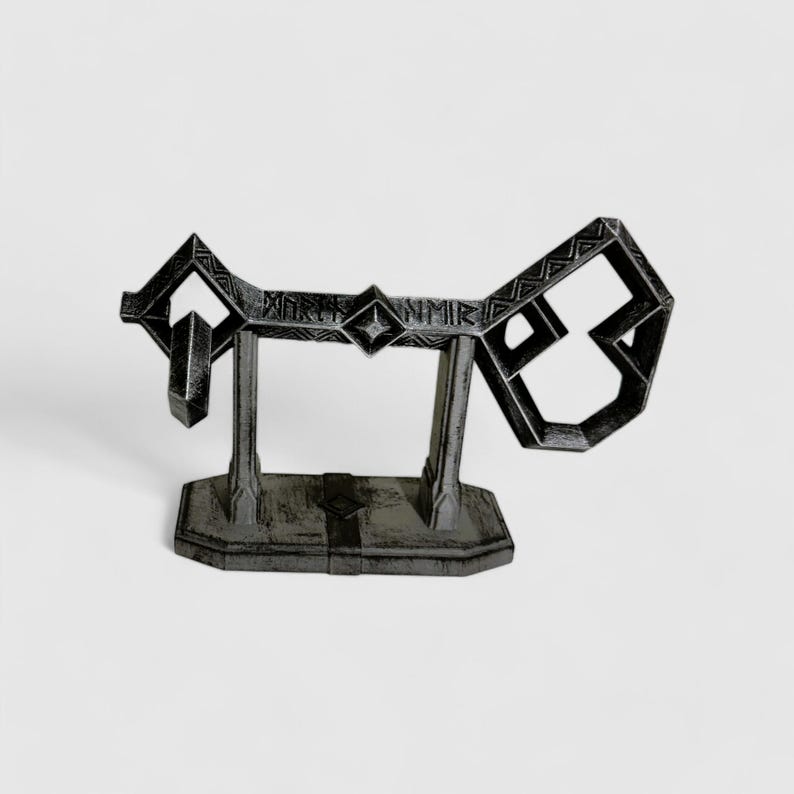 May include: A black metal key replica with intricate details and a decorative base. The key is shaped like a stylized letter 'J' and has a diamond-shaped design in the center. The base is rectangular and has a textured surface.