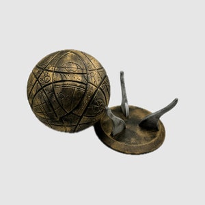 May include: A gold-colored sphere with intricate patterns and a matching stand with three legs. The sphere is decorated with a geometric design.