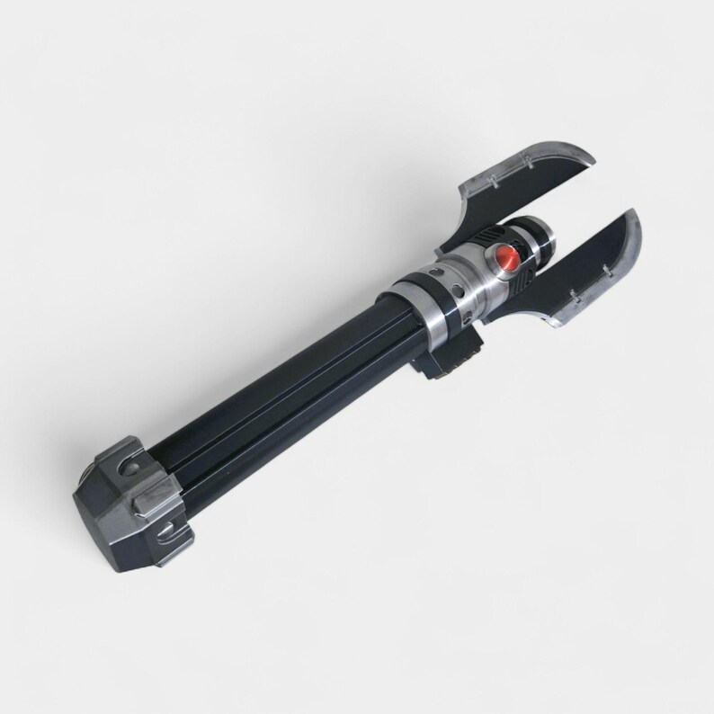 May include: A black and silver lightsaber prop with a red button and two curved blades. The hilt is black with silver accents. The lightsaber is a prop from a science fiction movie.