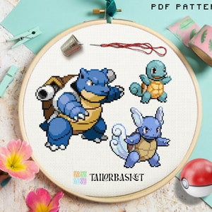 May include: Cross stitch pattern featuring three blue and brown Pokemon characters: Squirtle, Wartortle, and Blastoise. The pattern is displayed on a white embroidery hoop.