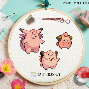 Könnte beinhalten: Ein Kreuzstichmuster mit drei rosa Pokémon-Charakteren, darunter ein Knuddeluff, ein Relaxo und ein Piepi. Das Muster ist in einem hölzernen Stickrahmen auf einem hellblauen Hintergrund dargestellt.