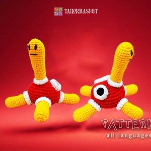 May include: Two crocheted amigurumi toys in the shape of a red and yellow creature with a long neck and four legs. The toys are on a red background. The text "PATTERN all languages" is at the bottom of the image.
