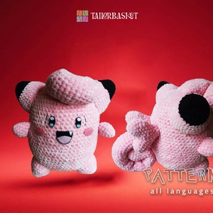 Könnte beinhalten: Rosa gehäkeltes Plüschtier eines Pokemon-Charakters, Jigglypuff, mit schwarzen Augen und einem lächelnden Mund. Das Spielzeug wird in zwei Posen gezeigt, eine mit ausgestreckten Armen und die andere mit eingerolltem Schwanz. Das Bild enthält auch den Text "PATTERN all languages" und ein Logo für "TAILOR BASKET".